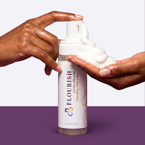 Styling foam bottle being pumped into brown hands against a purple background